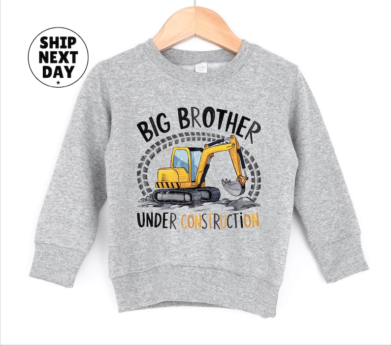 A gray sweatshirt with a graphic design featuring a yellow construction vehicle and the text "BIG BROTHER UNDER CONSTRUCTION" printed on it.