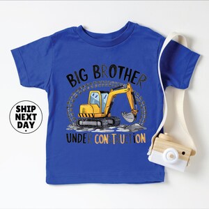 A blue t-shirt with a cartoon construction vehicle and the text "BIG BROTHER UNDER CONSTRUCTION" printed on it.