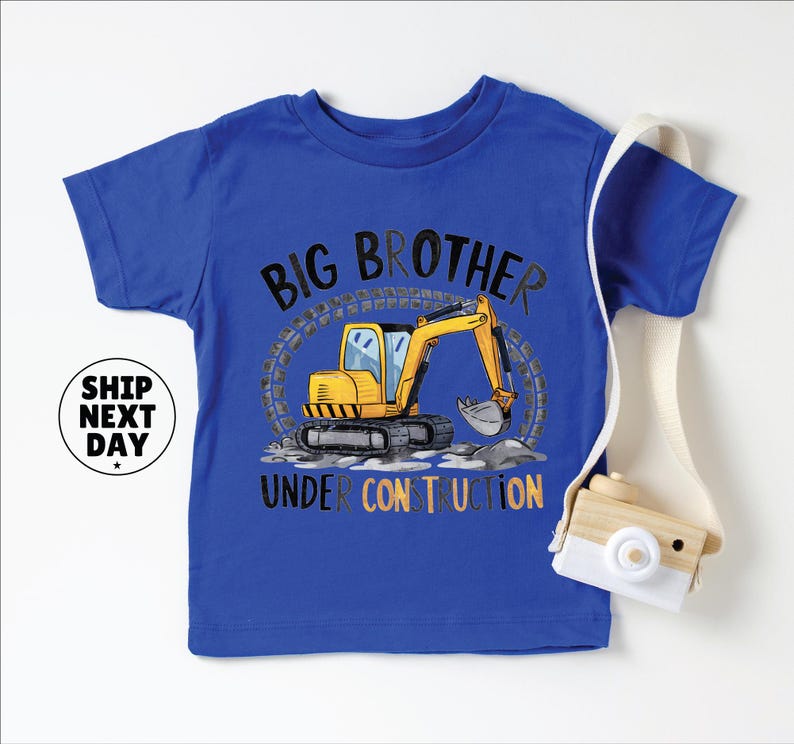 A blue t-shirt with a cartoon construction vehicle and the text "BIG BROTHER UNDER CONSTRUCTION" printed on it.