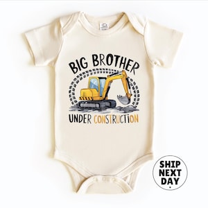 A baby onesie with a graphic of a yellow excavator and the text "BIG BROTHER UNDER CONSTRUCTION" printed on it.