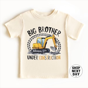 The image is a white t-shirt with a graphic design featuring a yellow construction vehicle and the text "BIG BROTHER UNDER CONSTRUCTION" printed on it.