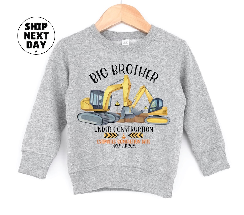 A gray sweatshirt with a graphic design featuring a construction site with a crane and a message that reads "BIG BROTHER UNDER CONSTRUCTION ESTIMATED COMPLETION DATE DECEMBER 2015".