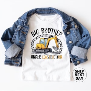 a white t-shirt with a graphic design of a yellow excavator and the text "BIG BROTHER UNDER CONSTRUCTION" printed on it, along with a denim jacket and a denim shirt.