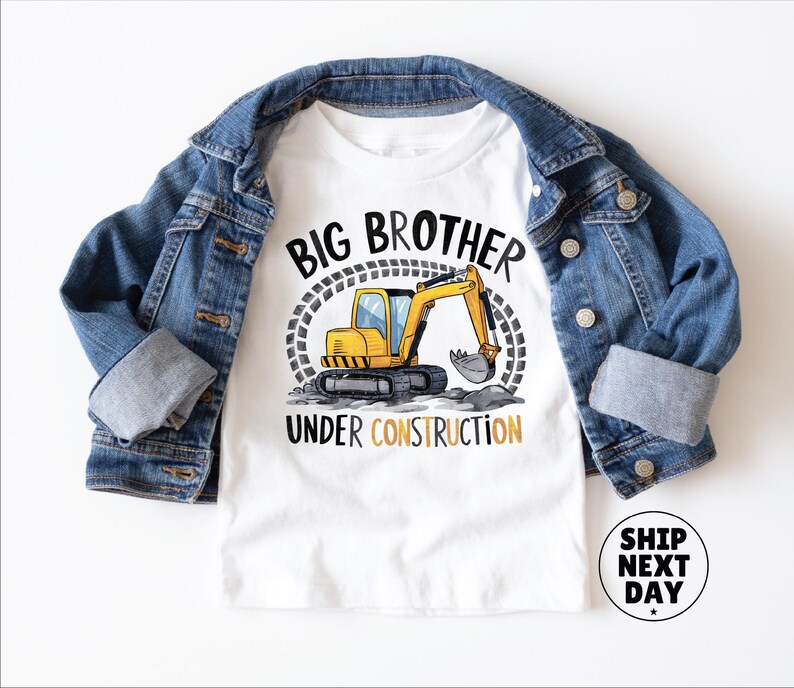 a white t-shirt with a graphic design of a yellow excavator and the text "BIG BROTHER UNDER CONSTRUCTION" printed on it, along with a denim jacket and a denim shirt.