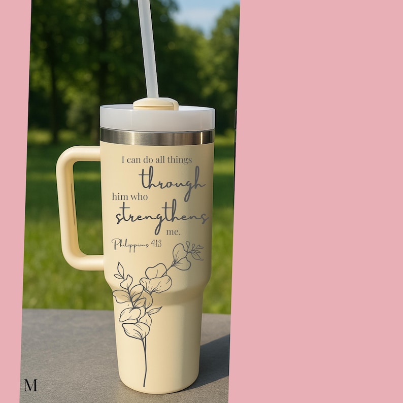 May include: A cream-colored tumbler with a handle and a white lid, featuring a straw. The tumbler has the text "I can do all things through him who strengthens me. Philippians 4:13" and a floral design.