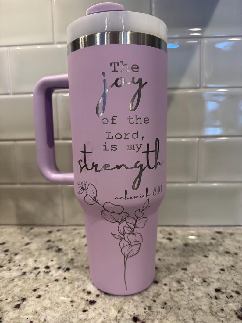 May include: A lavender insulated tumbler with a white and silver lid and handle. The text "The joy of the Lord is my strength" is displayed in silver script, along with a floral design and the reference "nehemiah 8:10".