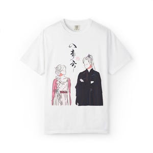 以下が含まれることがあります： 伝統的な衣装を着た2人の人物の線画イラストが特徴の白いTシャツ。デザインは、ピンクと白のドレスを着た女性と黒いローブを着た男性を示しています。シャツにはアジアの文字も含まれています。