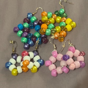 May include: Three pairs of beaded earrings in various colors. One pair features a mix of blue, green, and purple beads. Another has orange, yellow, and white beads. The third pair is pink and purple. All have silver-colored ear wires.