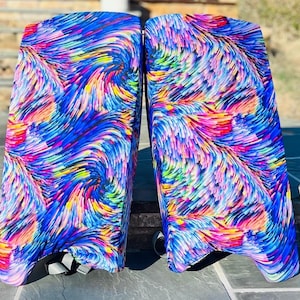 以下が含まれることがあります： 青、ピンク、黄色、紫の色合いで渦巻く筆致の鮮やかな多色抽象模様が特徴のアイスホッケー用ゴールキーパーレッグパッドのペア。パッドは滑らかで湾曲した表面を持ち、調節可能な灰色のストラップが付いています。