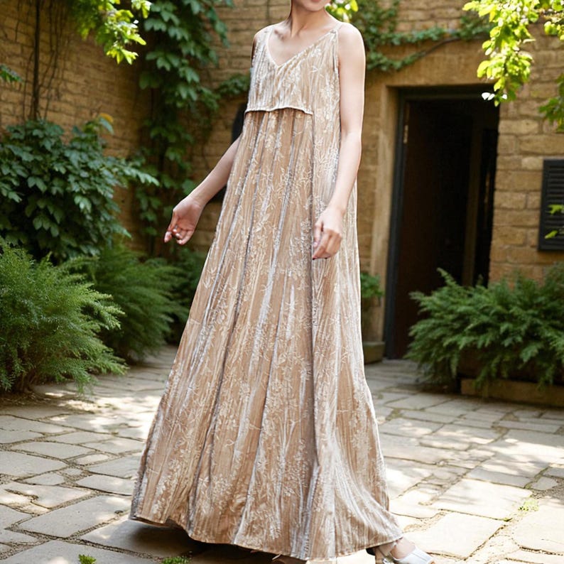 May include: A long, flowing, beige dress with thin straps and a V-neckline. The dress features a subtle floral pattern and a tiered bodice. The dress is made of a soft, flowing fabric, perfect for warm weather.