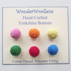 May include: A selection of six colourful, hand-crafted Yorkshire buttons. The buttons are in shades of pink, orange, yellow, green, red, and blue. The card reads "WonderWoollens Hand Crafted Yorkshire Buttons" and "Cotton Thread, Polyester Filling."