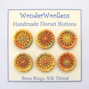 May include: Six handmade Dorset buttons in shades of yellow, orange, and green. The circular buttons feature a starburst pattern, crafted with brass rings and silk thread. The card reads "WonderWoollens Handmade Dorset Buttons".