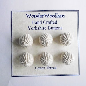 Puede incluir: Seis botones Yorkshire hechos a mano, de color blanquecino, hechos de hilo de algodón. Los botones son esféricos con una apariencia texturizada y tejida. La tarjeta dice "WonderWoollens Hand Crafted Yorkshire Buttons Cotton Thread."