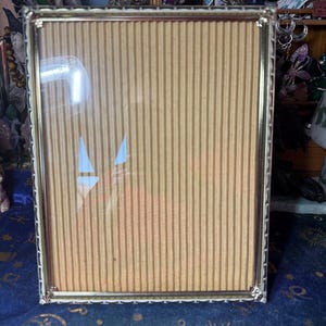 May include: A rectangular, vintage-style photo frame with a gold-coloured metal frame and a clear glass front. The frame has a decorative, openwork design around the edges. The backing is made of corrugated cardboard. The frame is designed to hold a photograph.