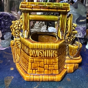 Può includere: Una fioriera a forma di pozzo dei desideri in ceramica nei toni del marrone e del verde. Il pozzo presenta un design a forma di mattone, un piccolo secchio e le parole "OH WISHING" sulla parte anteriore.