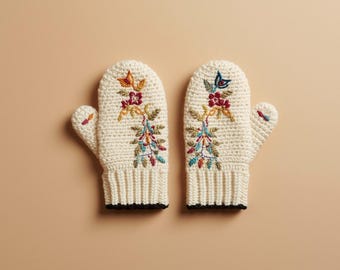 以下が含まれることがあります： クリーム色のミトン一組。刺繍された花と蝶のデザインが施されています。ミトンはリブ編みの袖口で、赤、オレンジ、青、緑の色合いのカラフルな糸で飾られています。背景は無地のタン色です。