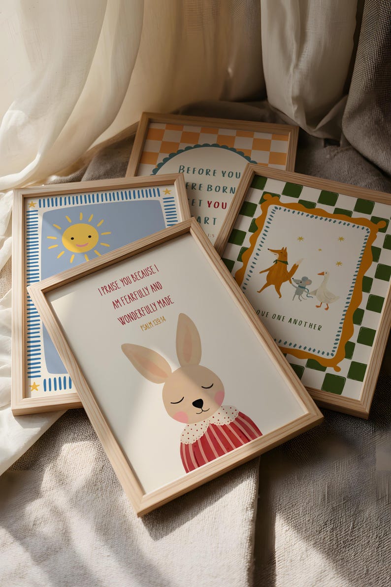 May include: A collection of framed art prints with light wood frames. The prints feature illustrations of a smiling sun, a bunny, and other whimsical designs. One print has the text "I PRAISE YOU BECAUSE I AM FEARFULLY AND WONDERFULLY MADE".