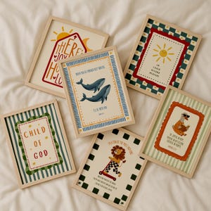 May include: A collection of framed art prints with various designs and text. The prints feature illustrations of a sun, whales, a lion on a scooter, and a goose reading a book. The frames are light wood.