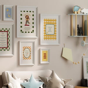 May include: A collection of framed art prints with white frames, featuring various designs and text. The prints include a lion on a scooter, a checkered pattern, and inspirational quotes. The color palette includes green, red, yellow, and blue.