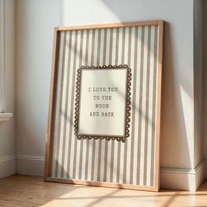 Può includere: Una stampa incorniciata con una cornice in legno marrone chiaro. La stampa ha uno sfondo a righe e un design rettangolare centrale con il testo "I LOVE YOU TO THE MOON AND BACK".