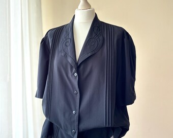 Camicetta nera vintage anni '80 con colletto ricamato e dettaglio a pieghe sulle spalle.