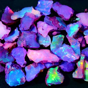May include: A collection of rough opal gemstones in shades of purple, pink, and blue. The opals have a natural, irregular shape and exhibit a play of color, with flashes of green and yellow. The image is well-lit, showcasing the gemstones' unique textures.