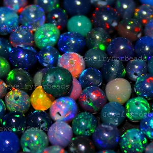 Peut inclure: Gros plan sur un assortiment de perles d'opale iridescentes de différentes couleurs, notamment le bleu, le vert, l'orange et le violet. Les perles sont rondes et brillantes, avec le texte "Jewelryforbeads" visible.
