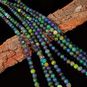 May include: Strings of iridescent opal beads in shades of blue, green, and purple. The beads are round and polished. They are displayed on a piece of textured, brown wood against a black background.