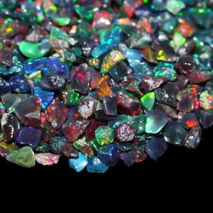May include: A close-up of a collection of rough opal gemstones. The opals exhibit a spectrum of colours, including blue, green, red, and orange, against a dark backdrop. The gemstones are irregularly shaped and have a natural, unpolished appearance.