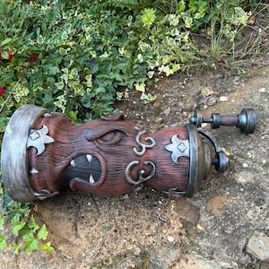 May include: A detailed, brown and gray decorative object with a unique design. The object has a cylindrical body with ornate carvings, metal accents, and a handle. The design includes stylized floral shapes and a textured surface.