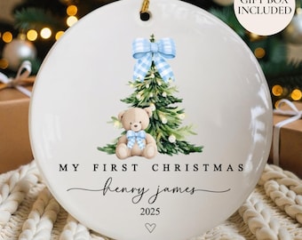 Könnte beinhalten: Weißer Keramik-Weihnachtsschmuck mit Aquarelldesign. Mit Weihnachtsbaum, Teddybär und blauer Schleife. Der Text lautet "MY FIRST CHRISTMAS" und "henry james 2025". Inklusive goldener Schnur zum Aufhängen.