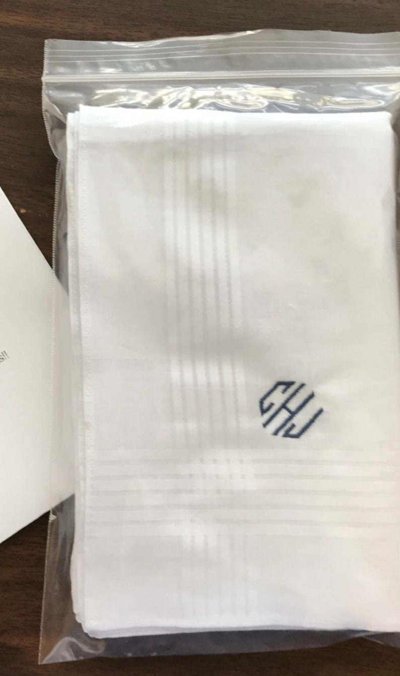 May include: A white handkerchief with a blue monogram of the letters "GHJ" in a circle. The handkerchief is folded and packaged in a clear plastic bag.