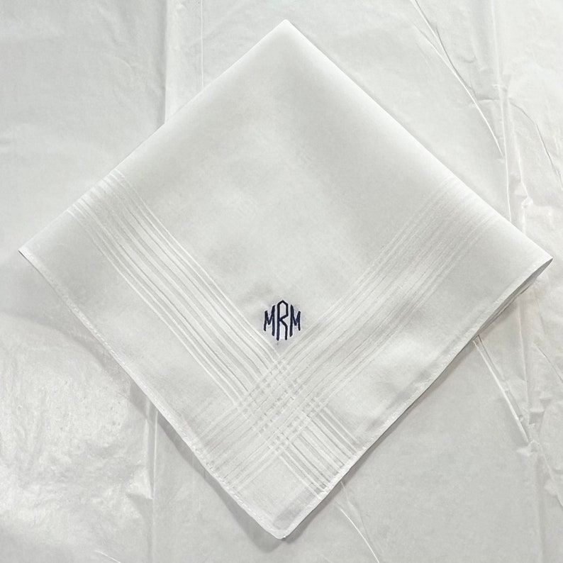 May include: White cotton handkerchief with a monogram of the initials "MRM" embroidered in navy blue.