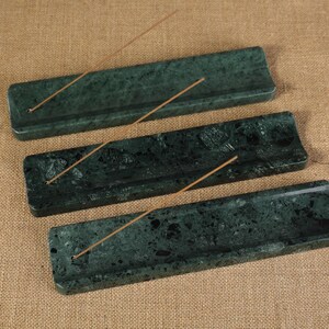 May include: Three dark green marble incense holders with a speckled pattern. Each rectangular holder has a small hole for incense sticks and a groove to catch ash. Incense sticks are placed in each holder.