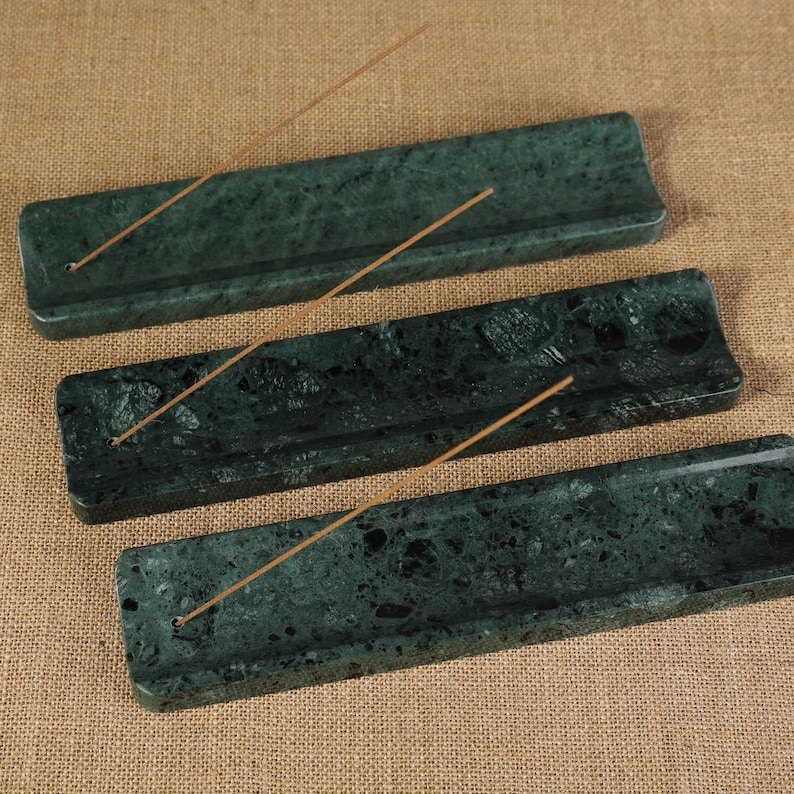 May include: Three dark green marble incense holders with a speckled pattern. Each rectangular holder has a small hole for incense sticks and a groove to catch ash. Incense sticks are placed in each holder.