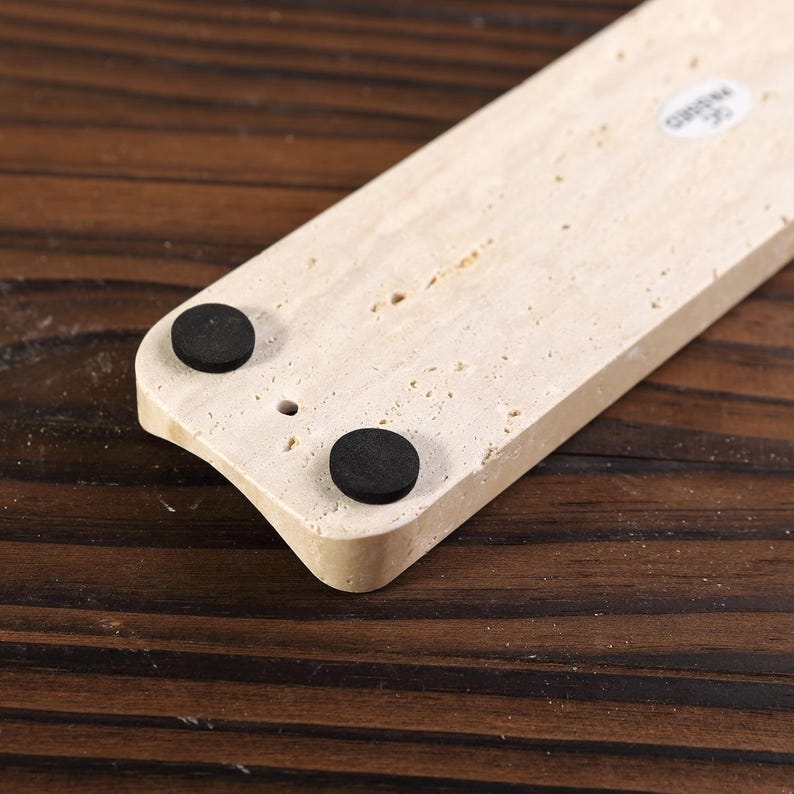 May include: A light beige rectangular incense holder with two black circular pads. The holder has a curved edge and a small hole. The surface has a textured appearance. The item is made of stone.