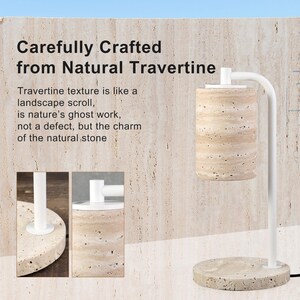 Op de afbeelding: Een kaarsverwarmerlamp met een cilindrische kap van natuurlijke travertijnsteen en een bijpassende ronde travertijnvoet. De lamp heeft een witte metalen arm en bovenbevestiging. De tekst op de afbeelding luidt: Carefully Crafted from Natural Travertine.