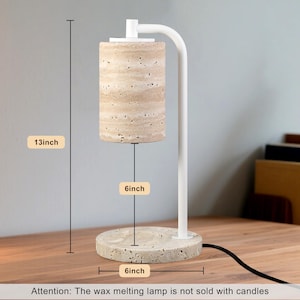 Op de afbeelding: Een kaarsverwarmerlamp met een wit metalen frame en een cilindrische kap van beige travertijnsteen. De voet is een bijpassende ronde travertijnsteen. De lamp is 33 cm hoog, met een voet van 15 cm en 15 cm ruimte voor een kaars.