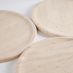 Puede incluir: Tres bandejas redondas beige con un borde ligeramente elevado. Las bandejas tienen un aspecto de piedra natural con vetas sutiles y peque&ntilde;as imperfecciones, lo que sugiere un material hecho a mano o natural. La paleta de colores neutros las hace vers&aacute;tiles.