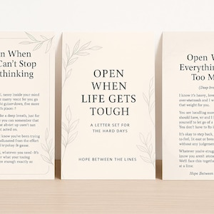 Peut inclure: Trois cartes crème avec du texte et des illustrations de feuilles. Les cartes indiquent "Open When You Can't Stop Overthinking", "Open When Life Gets Tough" et "Open When Everything Feels Too Much". Les cartes proviennent de "Hope Between the Lines".
