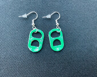 May include: A pair of handmade earrings featuring green pop-top charms with silver-colored ear wires. The green charms have a floral design. The earrings are displayed on a textured, dark blue surface.
