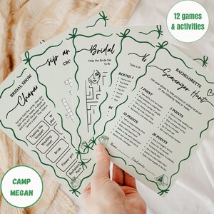 May include: A set of light green bachelorette party game cards with dark green decorative borders and text. The cards include games like Charades and a Scavenger Hunt. The text includes "12 games & activities" and "Camp Megan".