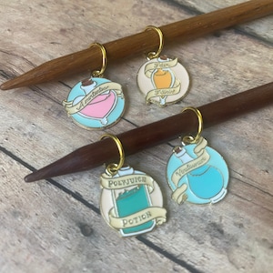 Könnte beinhalten: Vier bunte, potionflaschenförmige Maschenmarkierer mit goldenen Ringen. Die Markierer sind an zwei Holzstricknadeln befestigt. Die Potionflaschen sind mit "Felix Felicis", "A Momentus", "Veritaserum" und "Polyjuice Potion" beschriftet.
