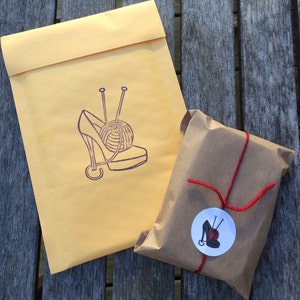 May include: A brown paper package tied with red string and a round sticker with a purple shoe and yarn ball design. The package is sitting on a wooden surface.