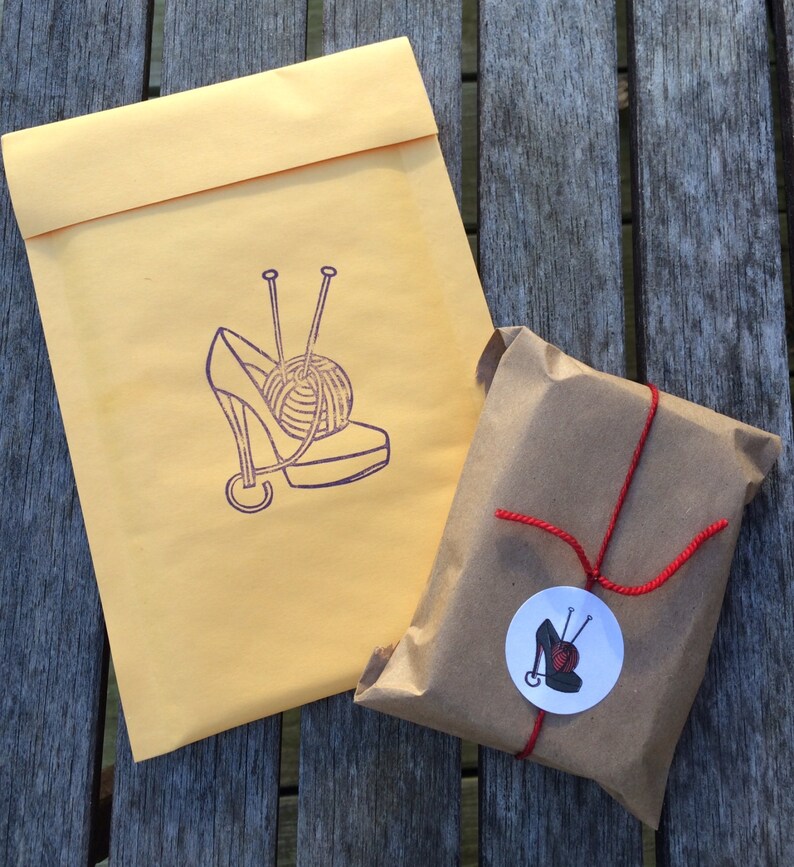 May include: A brown paper package tied with red string and a round sticker with a purple shoe and yarn ball design. The package is sitting on a wooden surface.