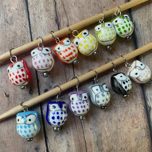 May include: A set of 10 colorful owl stitch markers. The owls are made of ceramic and have white bodies with different colored polka dots. The owls are attached to silver rings.