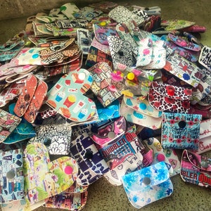 May include: A collection of colorful, patterned coin purses with various designs, including a cat, a dog, a skull, and a heart. The purses are made of fabric and have a button closure.