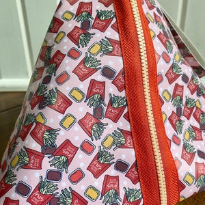 May include: A pink zippered pouch with a repeating pattern of red and white boxes with the words "fries over guys" and a graphic of french fries. The pouch has a red zipper with a white zipper pull.