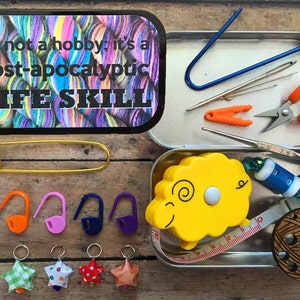 May include: A metal tin with a colorful yarn ball on the lid and the text "It's not a hobby; it's a post-apocalyptic LIFE SKILL". The tin contains various crochet and knitting tools, including a tape measure, scissors, stitch markers, and a yarn needle.