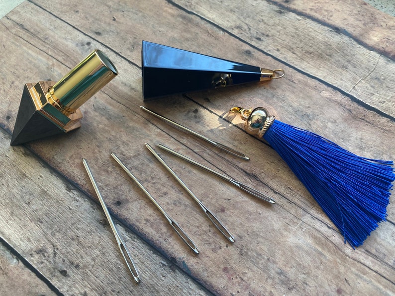 May include: A set of five silver needles, a black and gold lipstick tube, a black triangular box with a gold tassel, and a blue tassel.